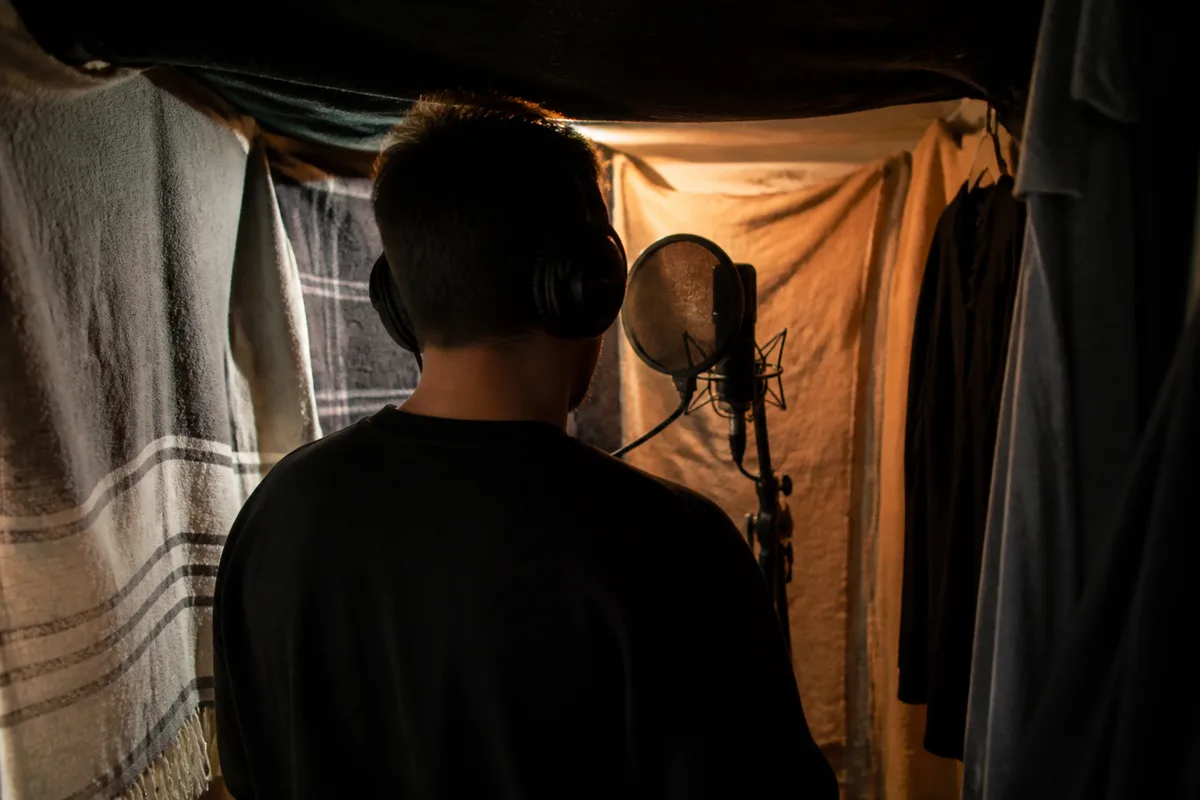 Chanteur devant un micro sur pied dans une chambre aménagée en studio, casque sur les oreilles